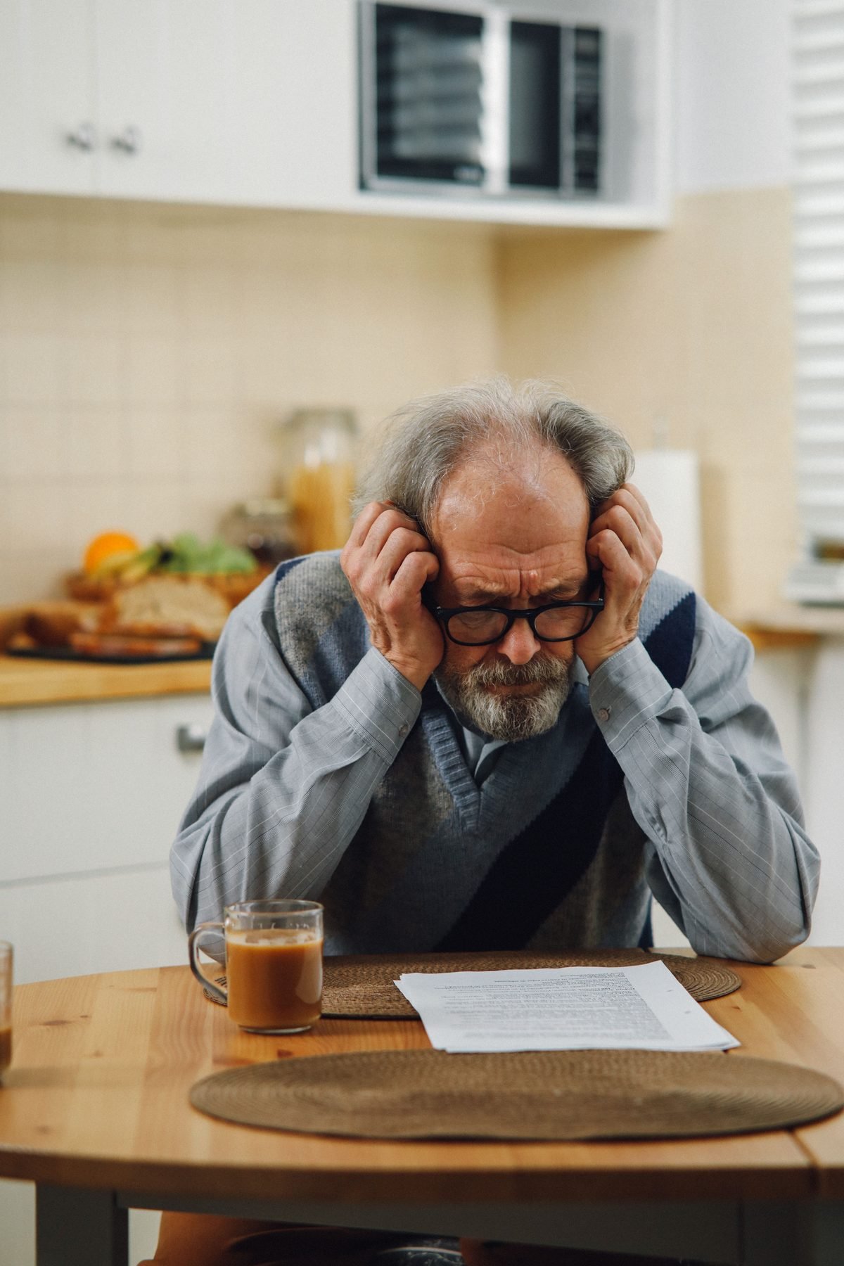 Worried older man sitting at his kitchen table with his head in his hands, concerned about enlarged prostate and urinary symptoms
